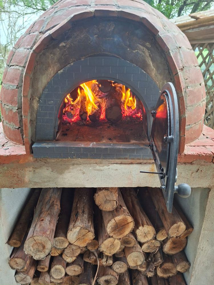 Forno revestido de tijolos, com a porta aberta e fogo aceso
