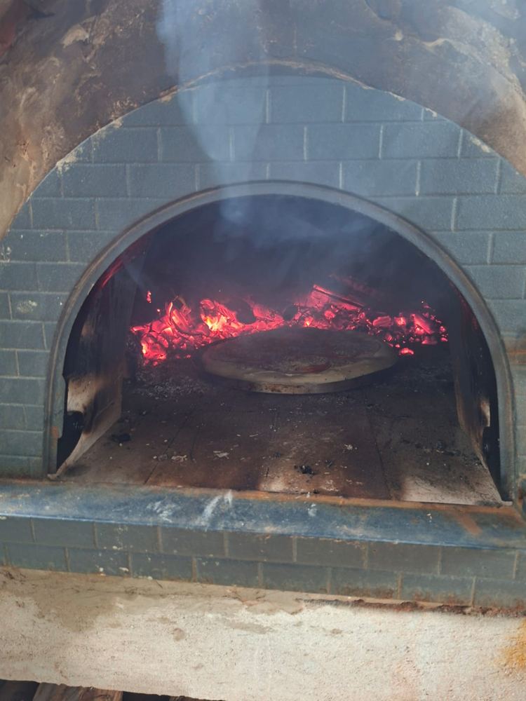 Pizza assando sobre as brasas dentro do forno